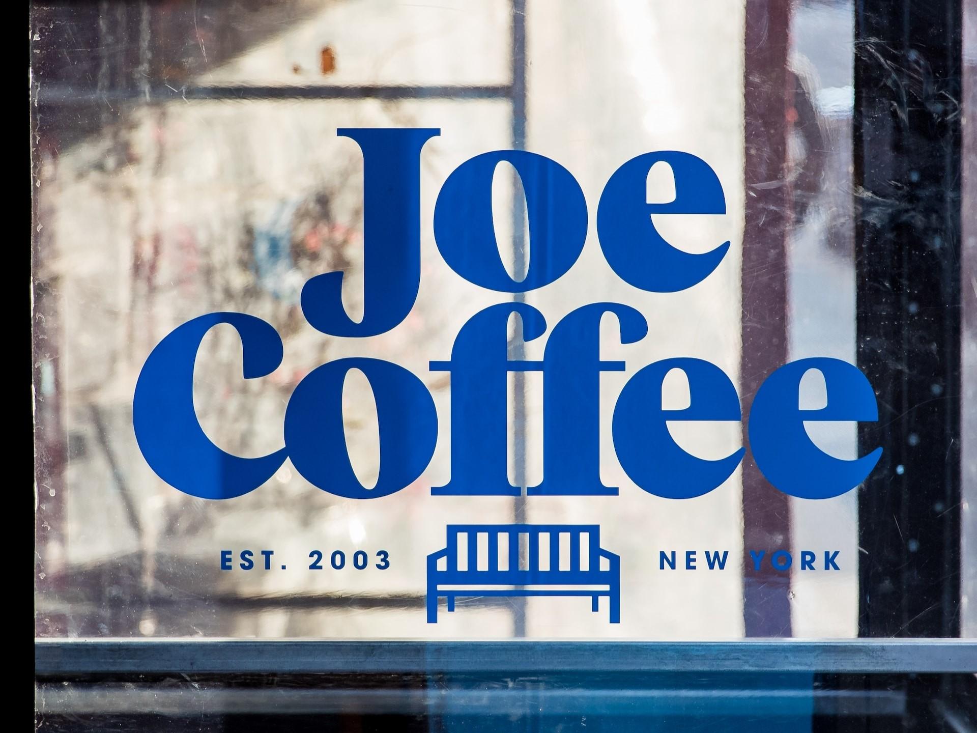 Joe Coffee New York Het logo van Joe Coffee in het blauw op een vitrineraam.